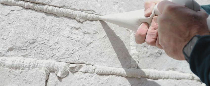 A close-up image of a professional applying grout between cultured stone pieces on an exterior wall in Edmonton, AB. The grout is evenly spread, and the surrounding stones are being sealed to protect against moisture and weather damage.