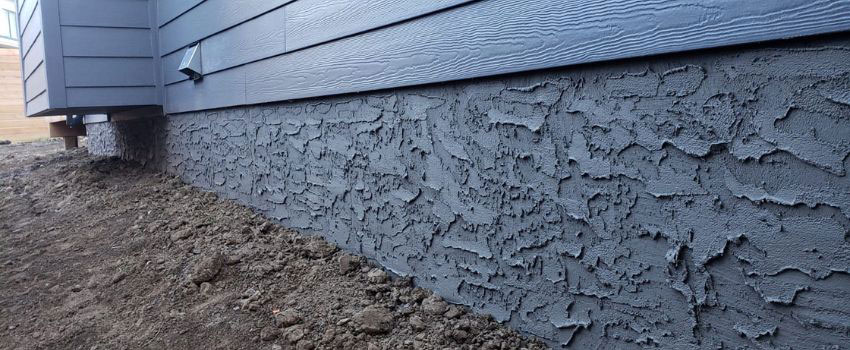 A homeowner inspecting the parging on their home’s foundation wall in Edmonton, AB, for cracks and signs of wear. Proper maintenance includes cleaning, sealing, and repairing minor damage to ensure the parging remains durable and effective.