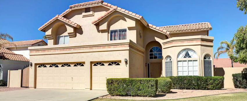 A homeowner in Edmonton, AB cleaning the exterior stucco walls of their house with a soft brush and hose to remove dirt and grime, preserving the stucco's appearance and durability.