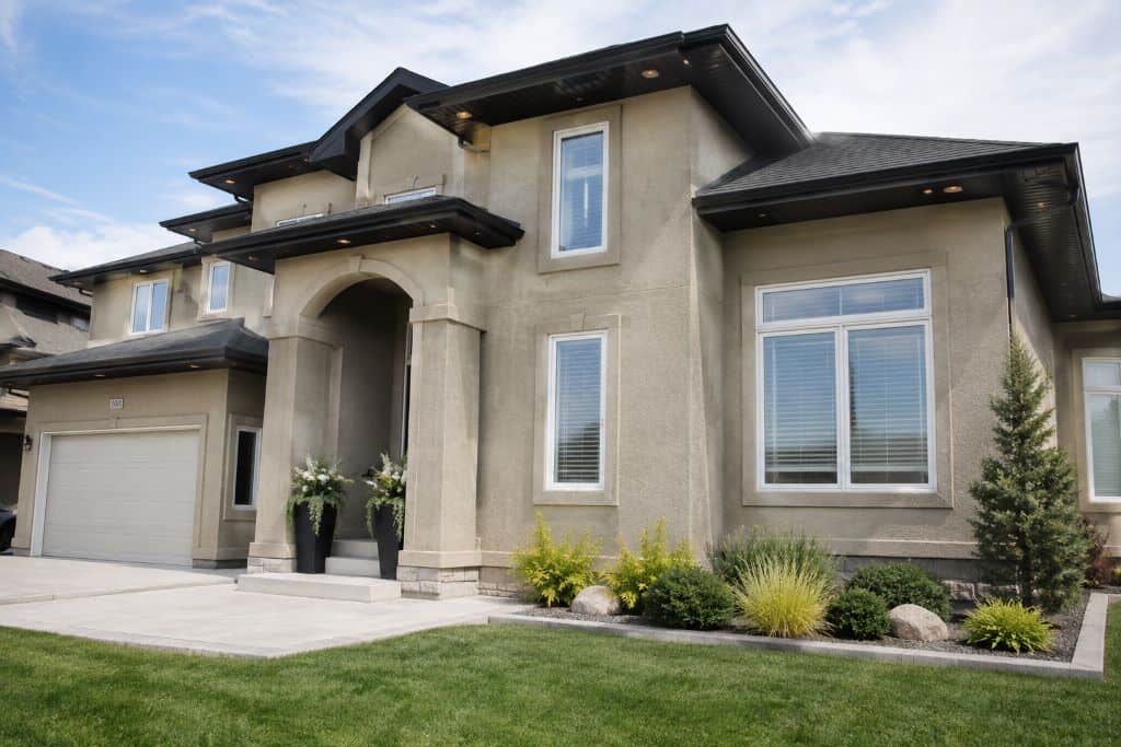 Finished two-storey home with textured stucco exterior, masonry accents, black rooflines, and landscaped front yard.