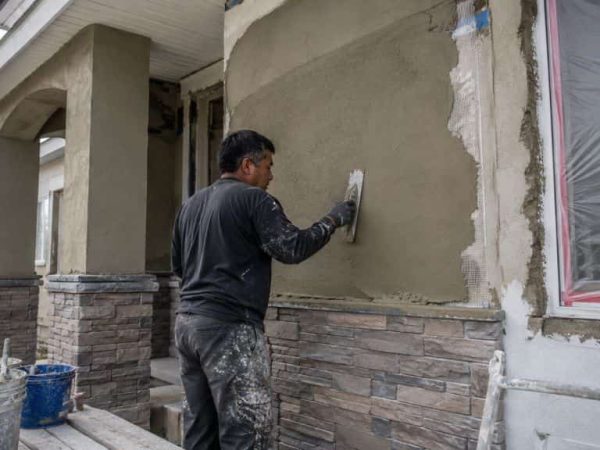 Contractor applying stucco beside stone veneer on a residential exterior during renovation work in Greenfield.