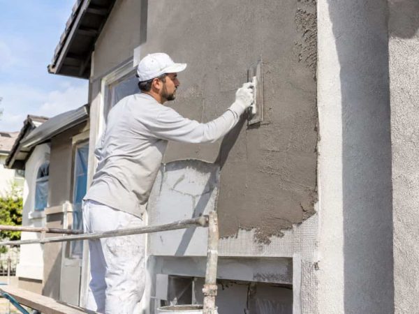 Contractor applying fresh stucco over reinforced mesh on a residential exterior wall in Mayliewan.